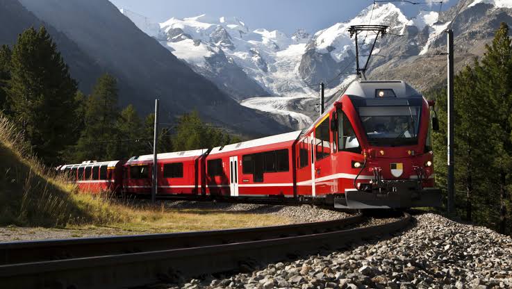Red passenger train travelling through snowy mountains